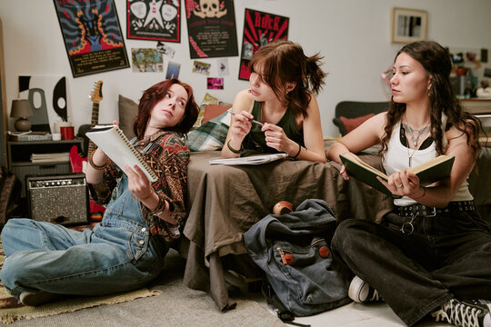 Teenage girls studying together in bedroom, writing notes and reading book while discussing homework, conveying collaborative learning. Ideal for education, youth study campaigns