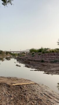 A view of calm water, trees, and a distant bridge at Wadi Al Aqeeq.