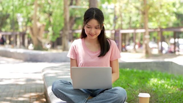 Smiling young asian young woman in university sitting outdoor working on laptop computer working or studying.