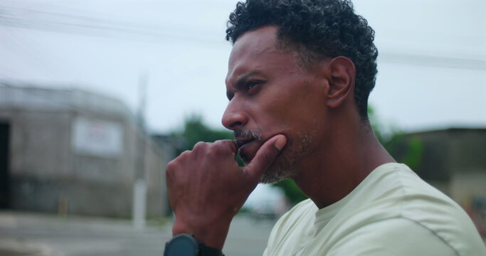 Hispanic Afro-Latin man with hand on chin, deep in thought, serious and focused expression, contemplating decision, outdoor urban setting, introspection, problem-solving