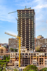 Fototapeta premium High-rise building in progress, cranes active, cityscape background, clear sky