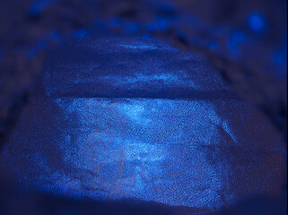 Bright blue light shines on a textured surface giving an interesting view of the space in the dark © Piotr