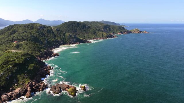 Aerial view of Joaquina rocky coastline with green hills and Atlantic waves in Florian&oacute;polis.