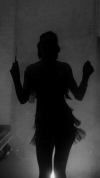 Old film style happy girl dancing, black and white color, dark female silhouette 20s 30s. vintage dress waving. flapper retro woman dancer at party night club room full smoke sexy body vertical video