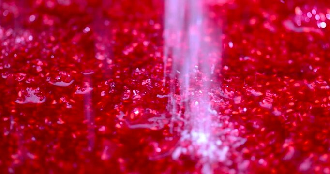 White sugar is sprinkled on red grated raspberries, white sugar grains fall in a stream onto the juicy texture of crushed raspberries in close-up