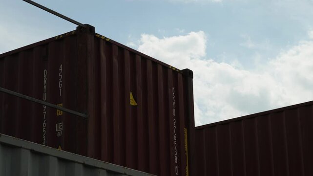  Large brown shipping containers standing under a cloudy blue sky.