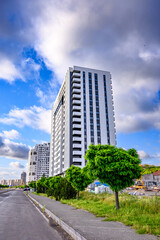 Obraz premium Tall white residential tower stands beside green trees and paved road
