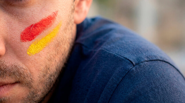 Close up of a male soccer fan with red and yellow face paint wearing a navy shirt