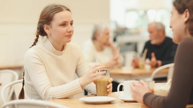Young woman with teen girl friend are spending time in cafe food court. Friend chatting and gossip while drink latte coffee, eating ice cream.