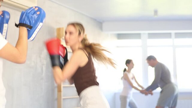 Woman wearing boxing gloves exercise and punch to pads for boxing. Woman with her trainer at gym. High quality 4k footage