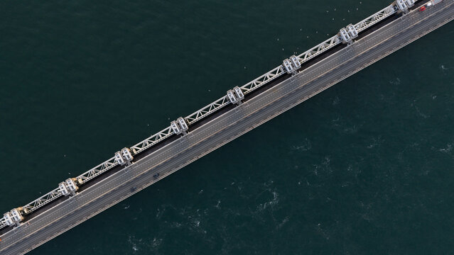 Aerial view of the Peilerdam storm surge barrier crossing the dark waters of the Oosterschelde, showing the structural steel gates and the road bridge in Burgh-Haamstede, Zeeland, Netherlands.