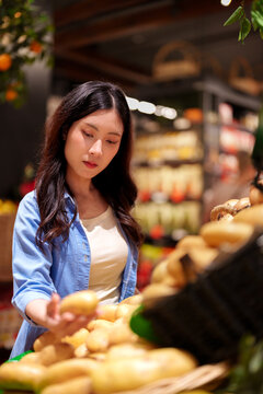 Young Asian woman selecting fresh bread at bakery display in supermarket shopping for groceries