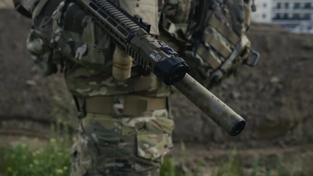 Camouflaged soldier in the middle of rural wilderness on a recon mission. Carrying an AR-15 carbine rifle with a red collimator and a magnifier