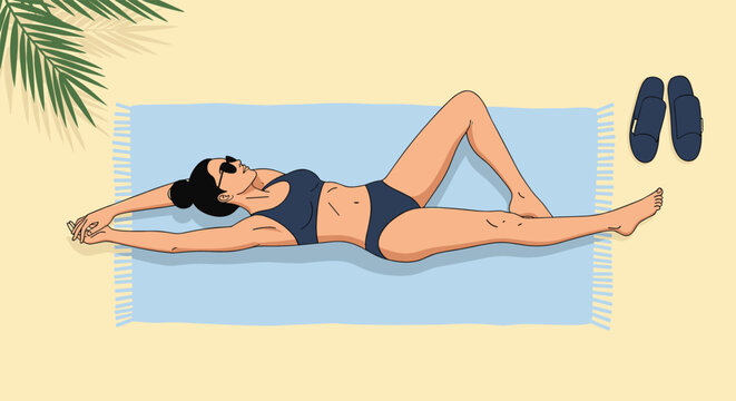 Young woman in a bikini relaxing on a blue towel at the beach while sunbathing under the shadow of a palm leaf on a bright summer day.