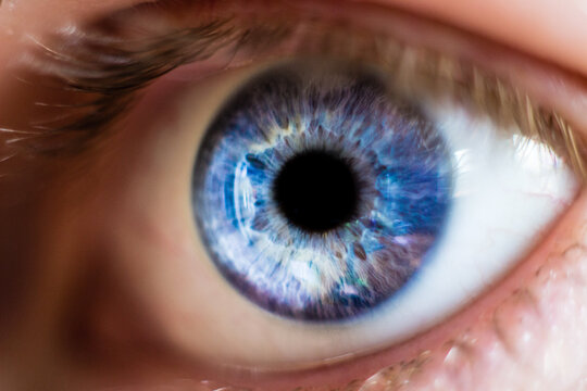 An extreme close-up macro photograph capturing the intricate textures and vibrant, varied blue hues of a human iris surrounding a dilated pupil.