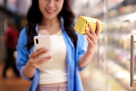 Young Asian woman holding golden gift envelopes while checking smartphone in modern shopping mall