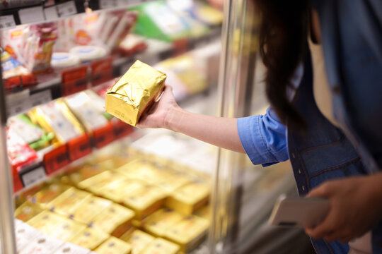 Young Asian woman selecting frozen food package from refrigerated display case in supermarket