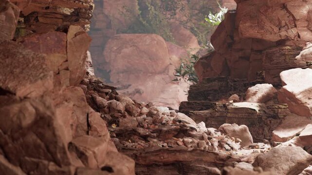 Rocks and boulders form a narrow path in a canyon. Sunlight filters through the opening, revealing greenery and the texture of the stones. Dust particles float in the air.
