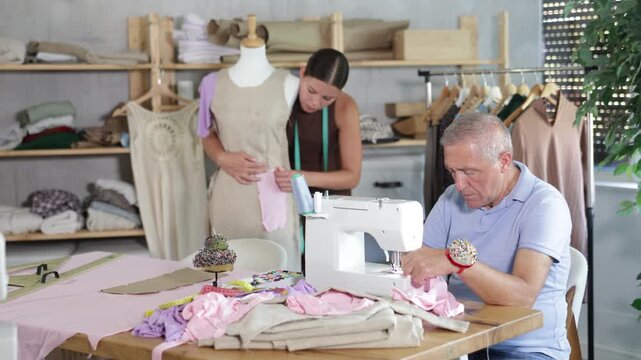 Elderly man tailor sews on machine young woman assistant sews on mannequin in workshop