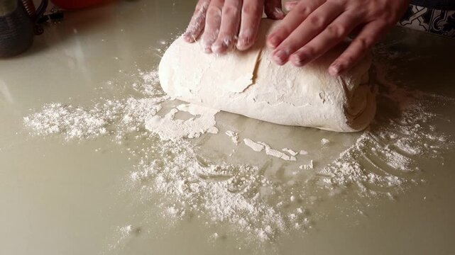 A baker's hands skillfully work a ball of dough, stretching and folding it on a surface dusted with flour, captured in smooth slow motion