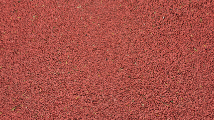 A top-down view shows the uniform, rough-textured surface of a reddish-brown rubberized running track or playground flooring. © aura