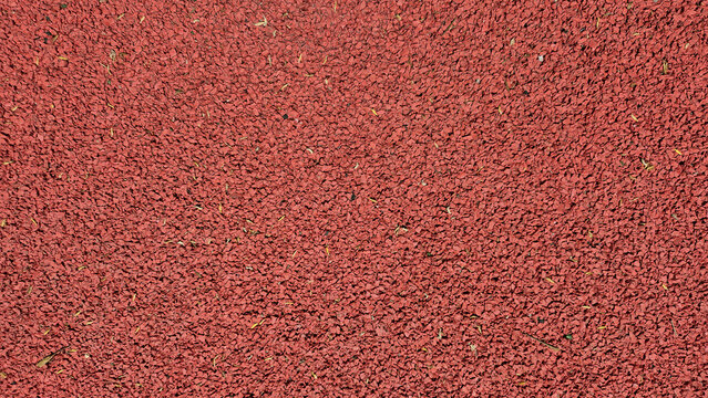 A top-down view shows the uniform, rough-textured surface of a reddish-brown rubberized running track or playground flooring.