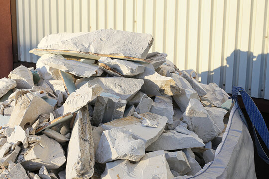 Construction demolition waste pile near industrial building. Broken insulation boards and rubble create textured background. Building renovation generates heavy debris. Recycling and disposal concept.