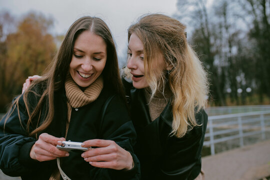 Female friends taking photos with vintage digital camera in autumn park