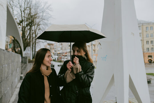 Female friends sharing umbrella on rainy autumn day in city