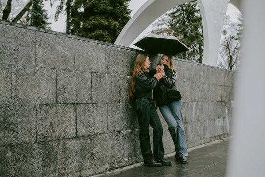 Female friends sharing umbrella on rainy autumn day in city