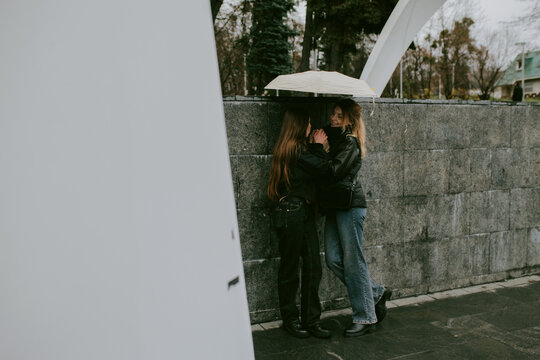 Female friends sharing umbrella on rainy autumn day in city