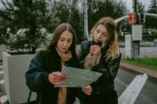 Female friends looking at paper map while traveling in rainy city