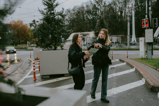 Female friends looking at paper map while traveling in rainy city
