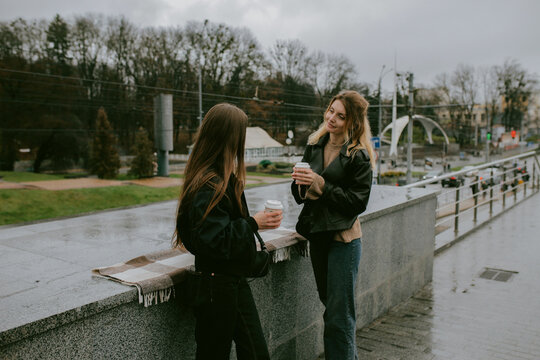 Two female friends drinking coffee outdoors on rainy autumn day