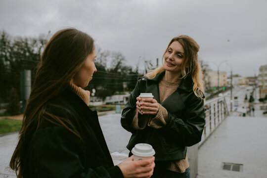 Two female friends drinking coffee outdoors on rainy autumn day