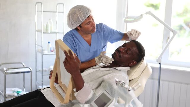 Male cosmetic doctor skillfully showcases remarkable results to his patient in mirror, revealing transformation that leaves patient in awe. High quality 4k footage
