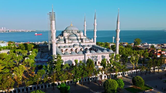 Aerial view of the Blue Mosque in Istanbul, Turkey. Sultanahmet Camii stands with six minarets, grand domes, green gardens and the blue sea behind.