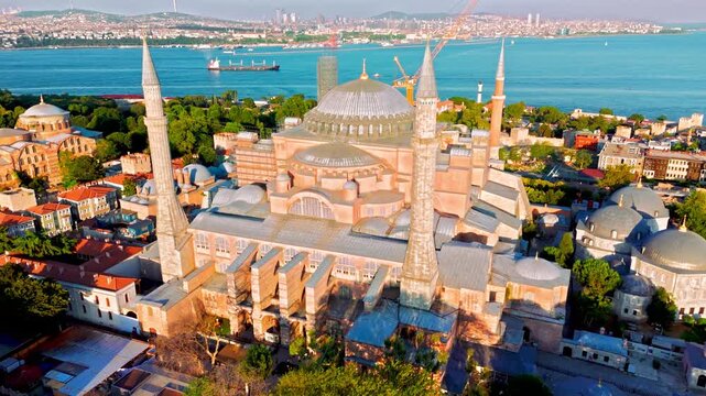 Aerial view of Hagia Sophia Grand Mosque in Istanbul, Turkey. The historic landmark stands with large domes and tall minarets near the Blue Mosque, Sultanahmet Square and the blue Bosphorus.
