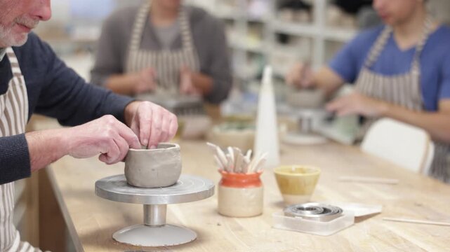 Close-up of elderly male hands carefully sculpting and shaping clay pottery piece on workbench in pottery studio
