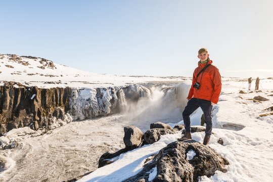 Man with camera standing at the edge, Selfoss waterfall in winter, gorge, northern Iceland, Iceland