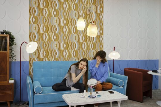 Young women engage in conversation while sitting on a couch in a stylish room and removing makeup