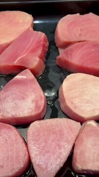 Pink tuna steaks on black tray, supermarket shelf closeup, chilled display of raw fresh fillets arranged in neat rows, subtle