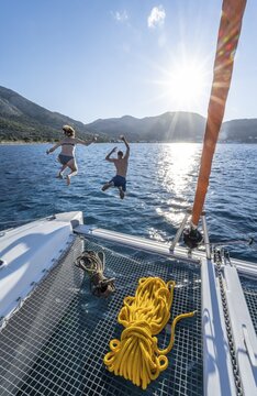 Young woman and young man jumping into the water, ropes on a sailing catamaran, Sun Star, sailing trip, Tilos, Dodecanese, Greece