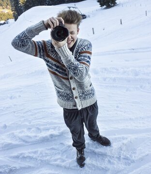 Young man in the snow taking a picture with a digital SLR camera, Hochbrixen, Brixen im Thale, Tyrol, Austria