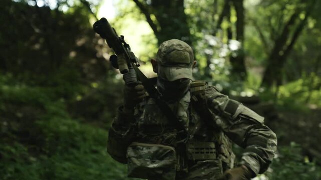 Camouflaged soldier in the middle of a dark forest on a mission. Reloading and aiming a AR-15 carbine rifle with a red collimator and a magnifier
