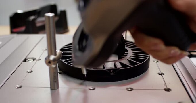 A hand using a handheld laser 3d scanner to digitize a physical black plastic mechanical component on a table