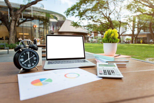 Outdoor Workspace with Laptop Blank Screen, Clock, Calculator, and Charts on Wooden Table in Park