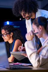 Low-light scene where a diverse, multiethnic software team share a moment over the laptop in a...