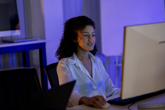 Woman computer office night desk monitor keyboard mouse professional technology, focused professional woman using computer at office desk during night shift under blue light in modern workspace