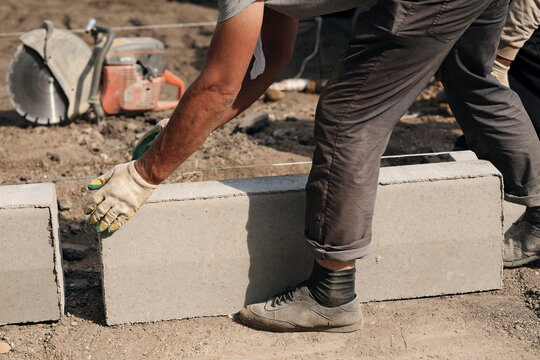 Construction worker manually adjusting concrete curb stone during sidewalk pavement installation. Perfect for road repair contractors, urban paving services, and masonry websites.